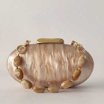 Clutch bag with gold chain and shell-like design on a light gray background, 