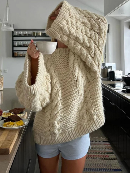 Person wearing a large beige knitted sweater in a kitchen