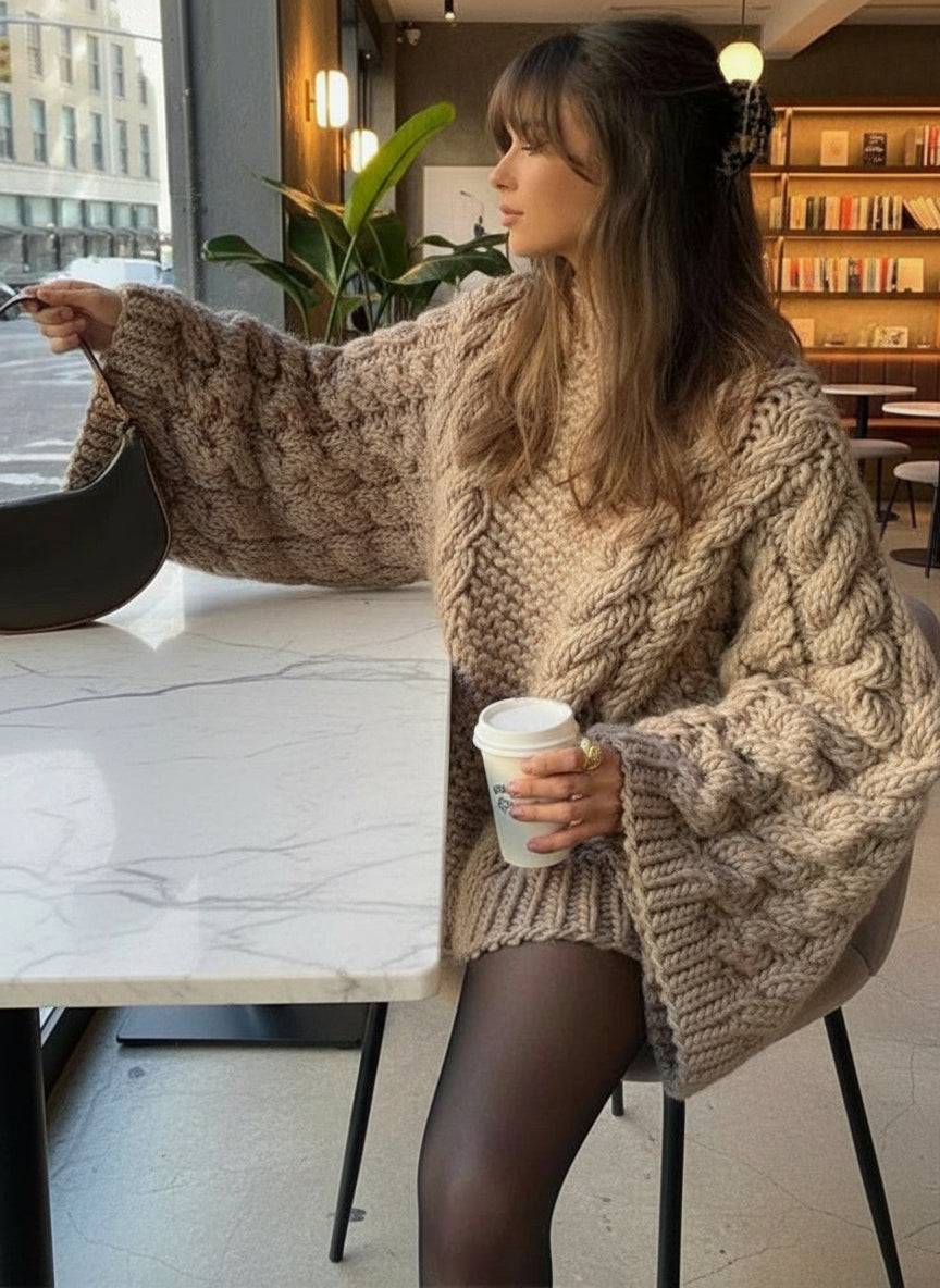 Woman in a cozy setting wearing a chunky knit sweater and UGG boots, holding a coffee cup.